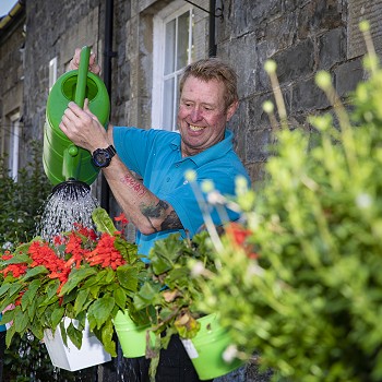 Man watering the flowers outside Cartref Bryn yr Eglwys