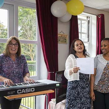Lady playing piano and two ladies singing to celebrate 35 years of Cartref Bryn yr Eglwys